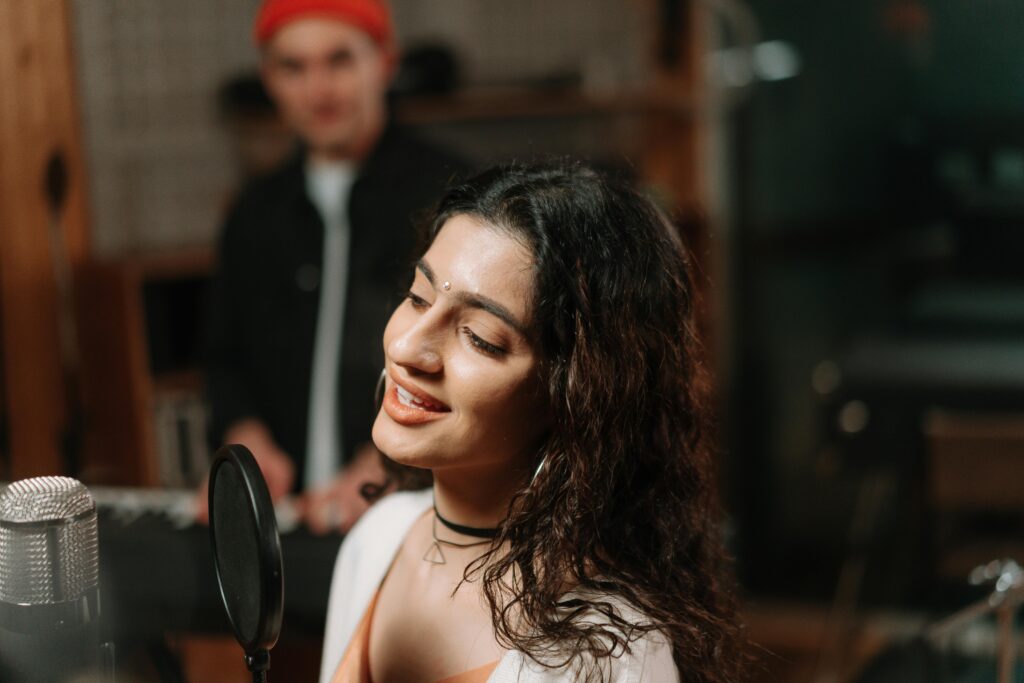 A joyful woman sings into a condenser microphone in a modern recording studio.